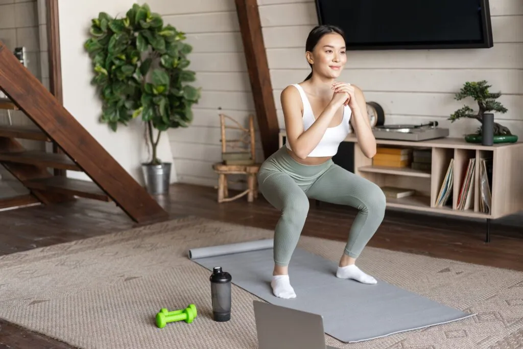 young asian fitness girl doing squats workout home follow online sport gym instructor standing